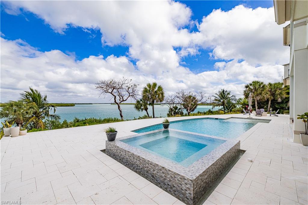 Expansive outdoor living area featuring a rectangular pool and integrated spa with mosaic tile surround, spacious paver patio, and tropical landscaping