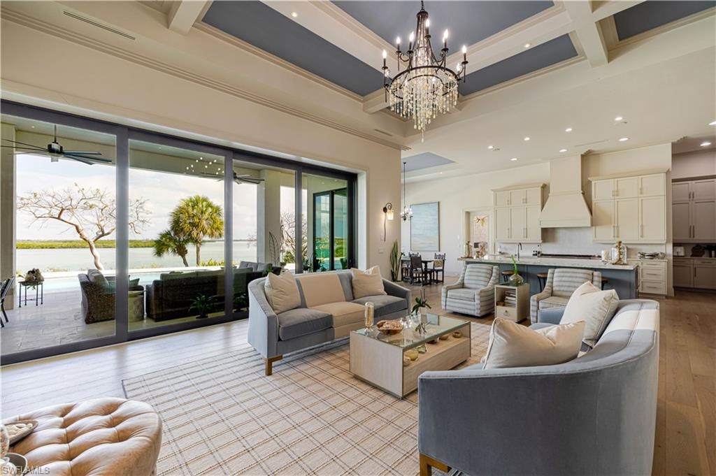 Open-concept living area featuring a coffered ceiling with a crystal chandelier, wood-finish flooring, and expansive sliding glass doors