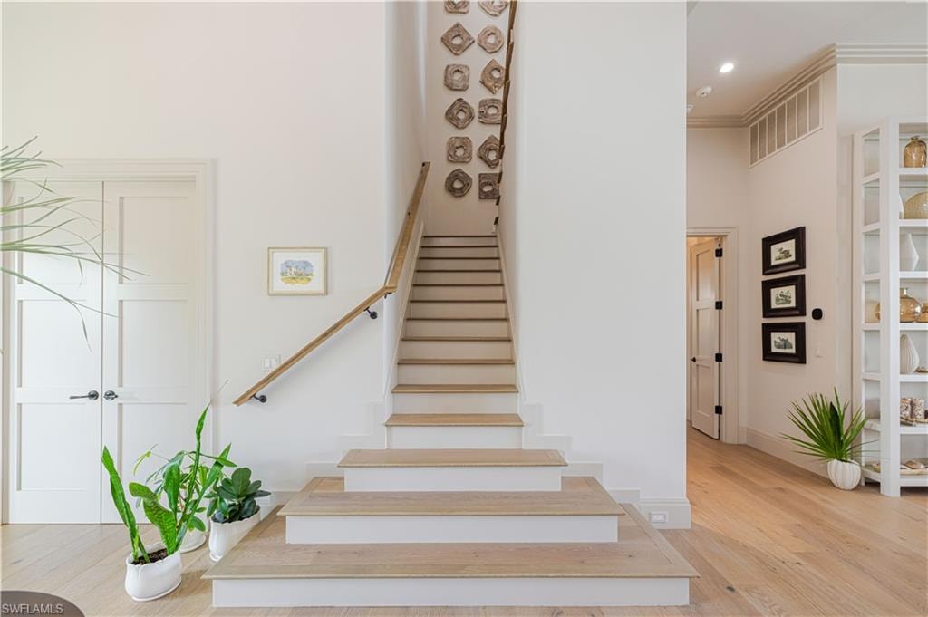 Grand entryway featuring light wood-finish flooring, a contemporary staircase with wooden handrail, recessed lighting, and built-in shelving