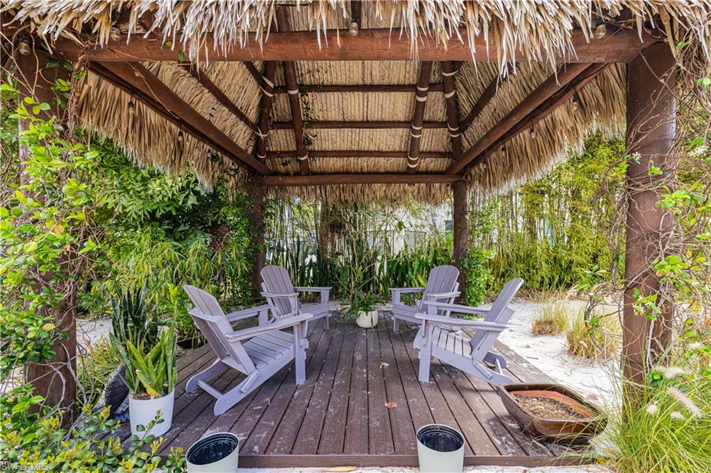 Thatched-roof gazebo with a dark wood-finish deck, surrounded by lush tropical foliage and white groundcover