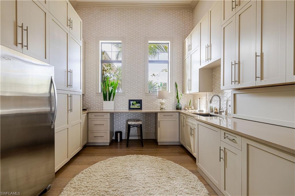 Dedicated utility space featuring extensive cabinetry, integrated desk area, under-cabinet lighting, a stainless steel refrigerator, and wood-finish flooring