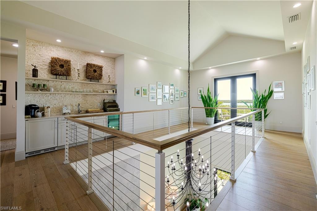Spacious upper-level landing featuring wood-finish flooring, a contemporary cable railing system, and a wet bar with stone-finish accent wall