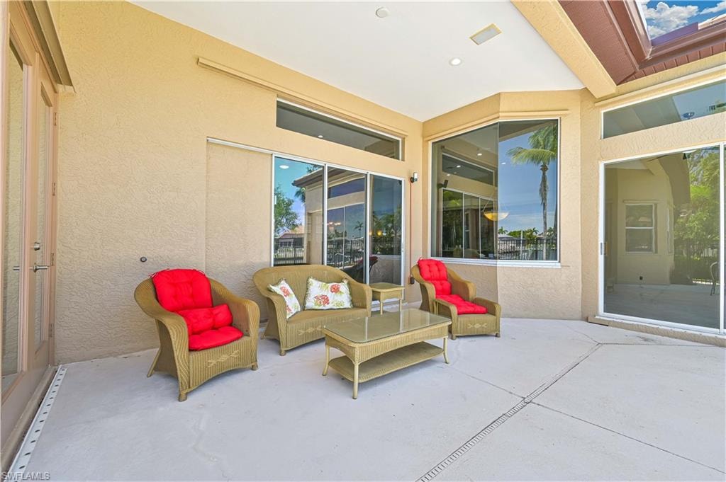 Spacious covered patio featuring textured stucco walls, multiple large windows, a glass-paneled door, and recessed lighting