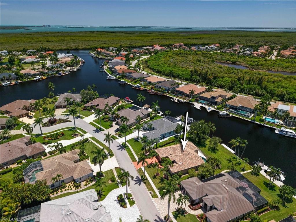 Waterfront property featuring a private boat dock, lush landscaping with mature palm trees, a spacious paved driveway, and a tiled roof