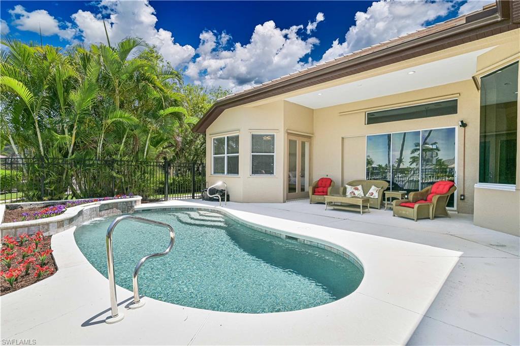 Curved swimming pool with integrated steps and a stainless steel handrail, surrounded by a concrete patio