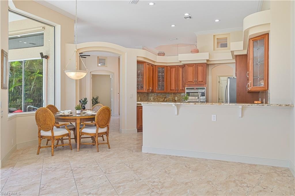 Open-concept living space featuring neutral tile flooring, a bay window, and a kitchen with wood cabinetry and a stone countertop
