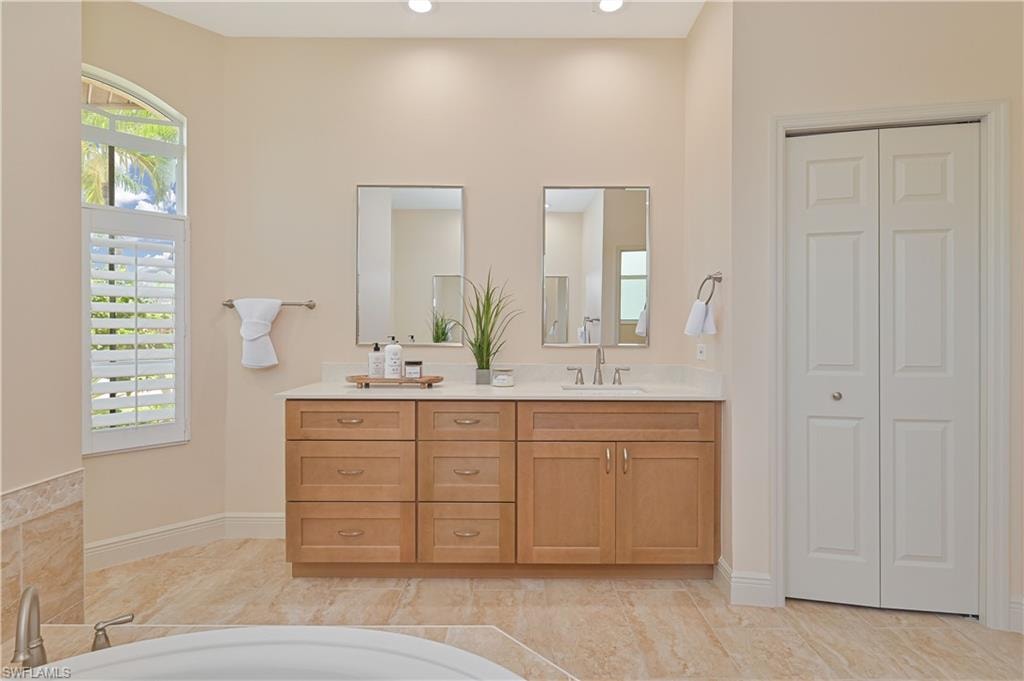 Double vanity featuring light wood-finish cabinetry, a light-toned countertop, and dual mirrors