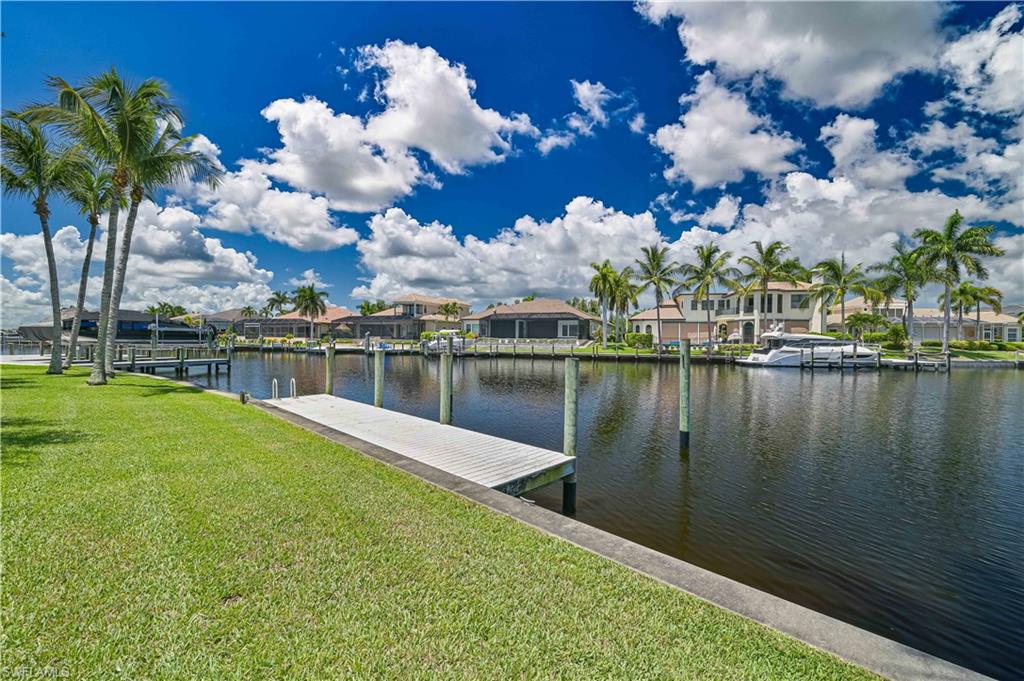 Waterfront property featuring a private dock, expansive green lawn, and mature palm trees