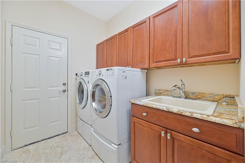 Laundry room with wood cabinetry, a utility sink set in a patterned stone countertop, and light-toned tile flooring