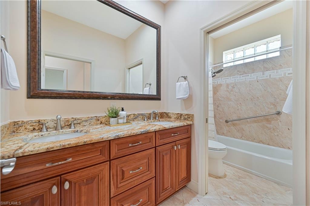 Bathroom featuring a dual vanity with a granite countertop, wood-finish cabinetry, and an ornate framed mirror
