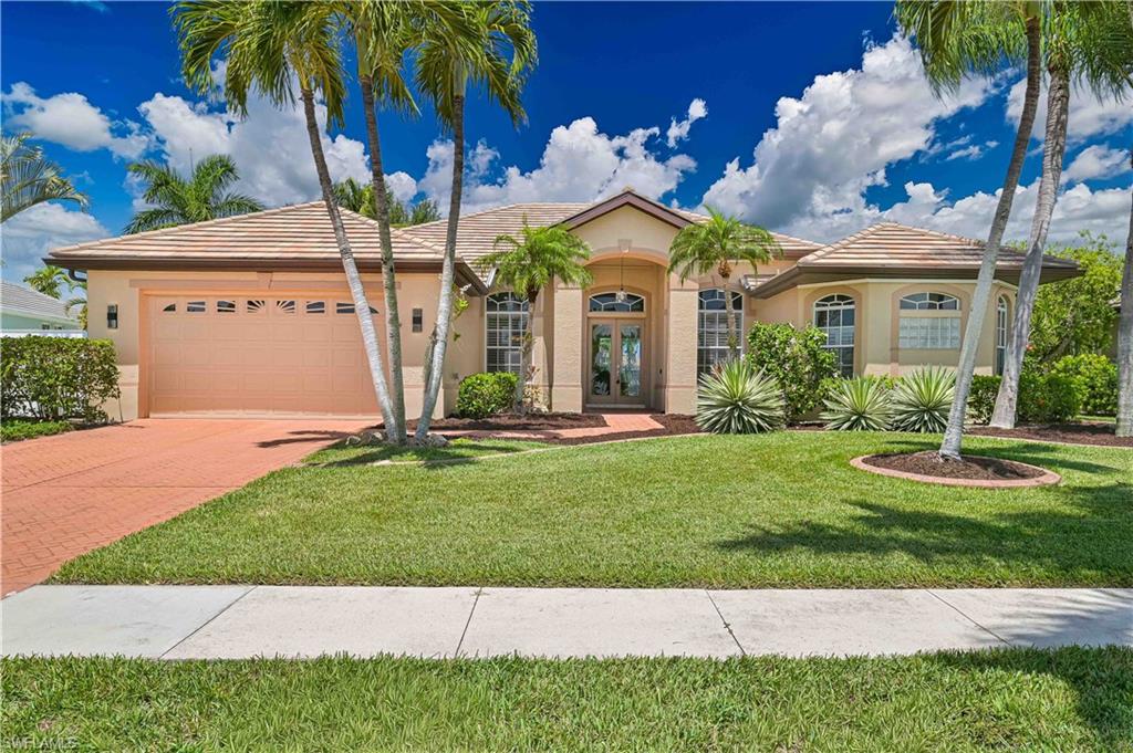 Symmetrical stucco exterior with a tile roof, arched entryway featuring double glass-paneled doors, and a paver driveway