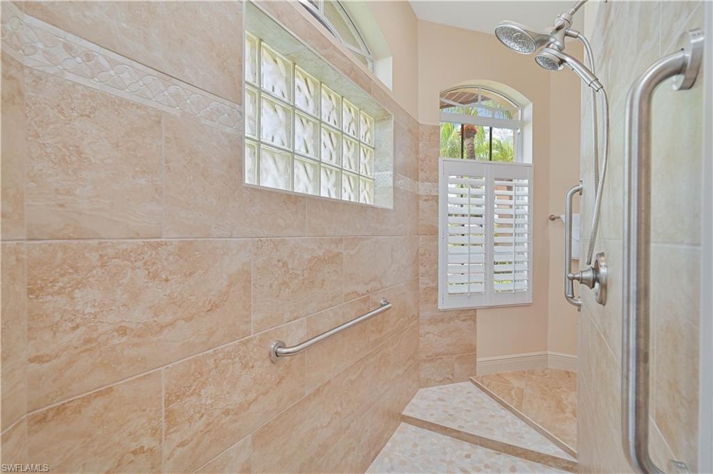 Walk-in shower with full-height tile surround, decorative tile accent band, glass block transom window, and a dual shower head system
