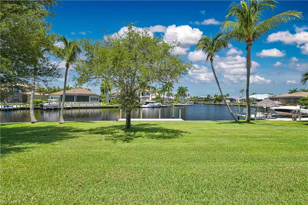 Expansive green lawn with mature trees and palm trees, bordering a canal with multiple boat docks