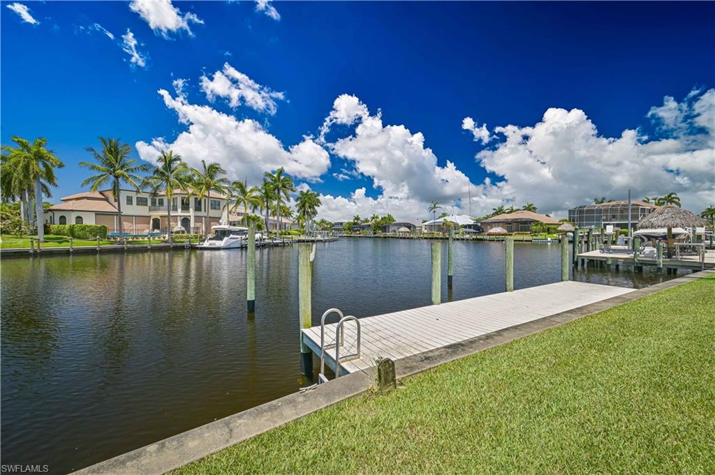Waterfront property featuring a private boat dock with a ladder, lush green lawn, concrete seawall, and mature palm trees