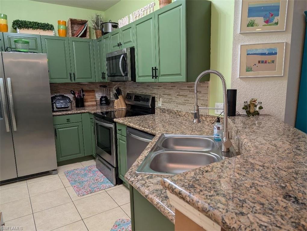Kitchen featuring stainless steel appliances, decorative backsplash, light tile patterned flooring, and green cabinets
