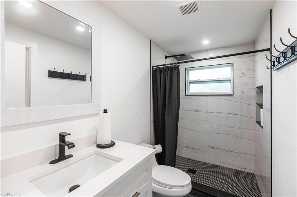 Bathroom featuring a single vanity with matte black faucet, a framed mirror, a tiled shower with a window, and recessed shelving