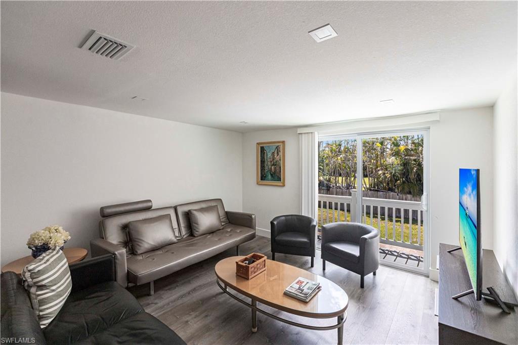 Living area featuring wood-finish flooring, white walls, recessed lighting, and sliding glass doors opening to outdoor space with a white railing