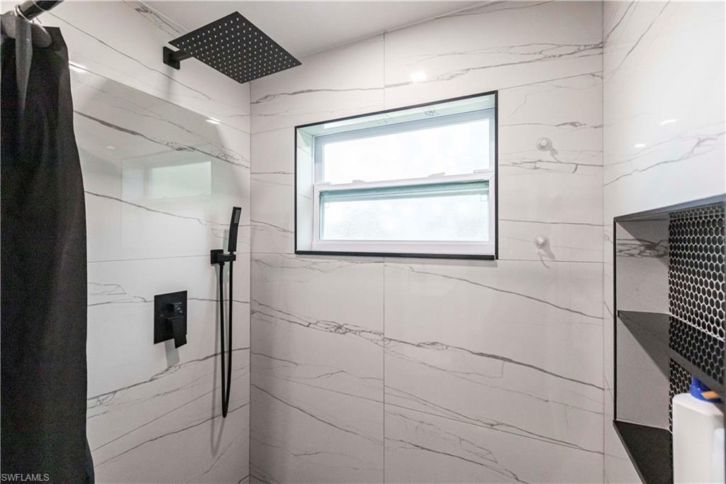 Shower featuring full-height white tile with gray veining, a matte black rainfall showerhead, a matte black handheld shower, and a built-in shower niche with black penny tile backing
