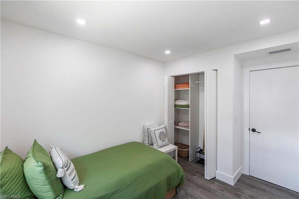 White-painted room featuring wood-finish flooring, recessed lighting, a built-in closet with shelving and a hanging rod, and a solid white door with a black handle