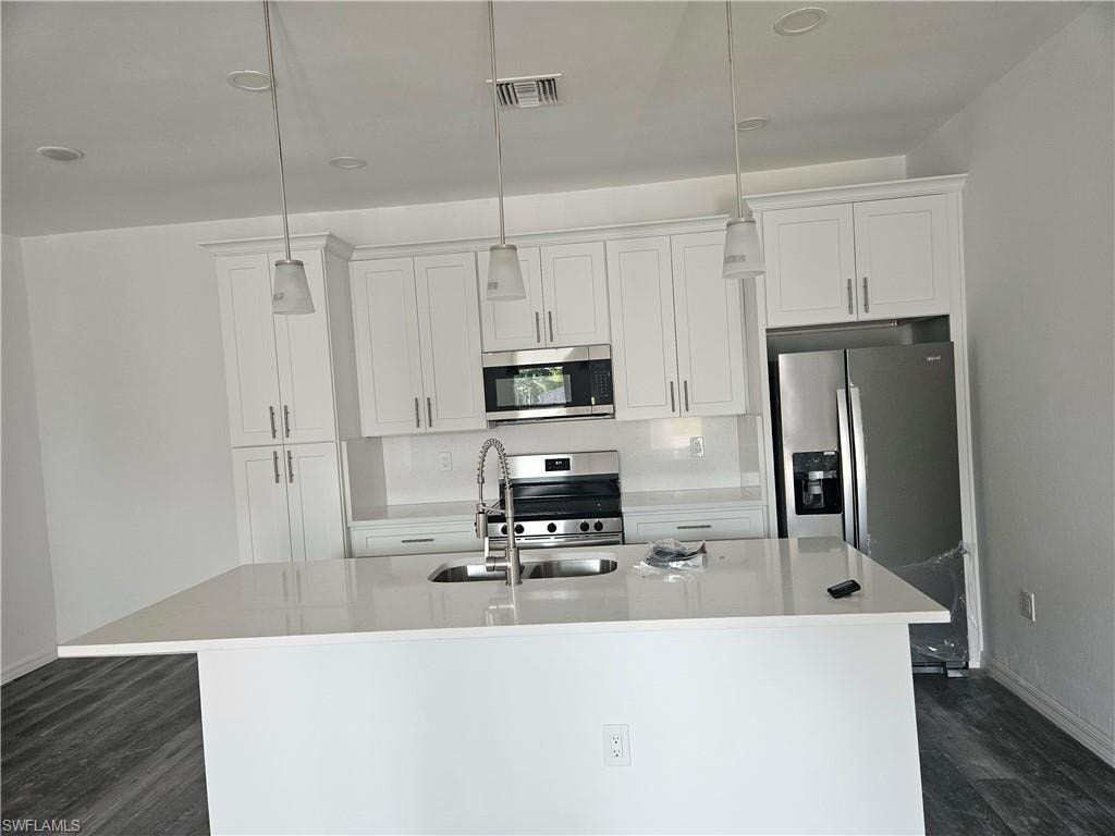 Kitchen with appliances with stainless steel finishes, a kitchen island with sink, dark wood-style flooring, and white cabinets
