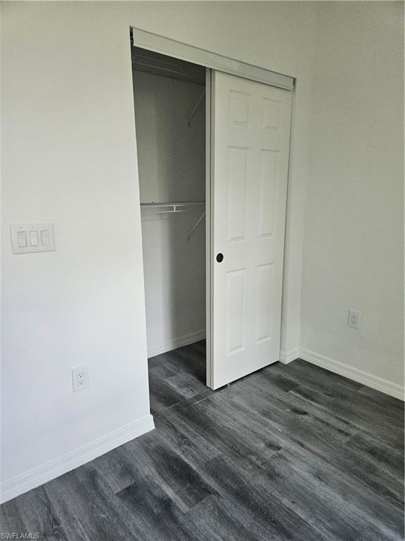Unfurnished bedroom with a closet, dark wood-style flooring, and baseboards