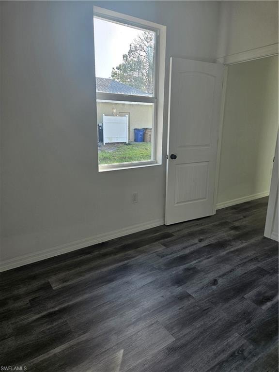 Empty room featuring baseboards and dark wood-style floors