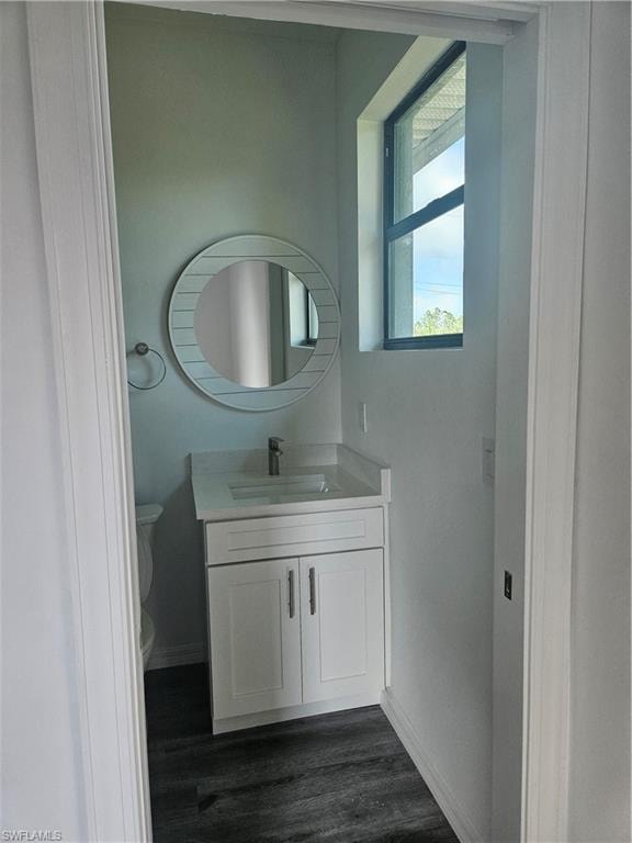 Half bath with baseboards, wood finished floors, toilet, and vanity