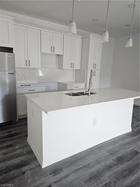 Kitchen featuring white cabinets, refrigerator, a center island with sink, a sink, and dark wood-style floors