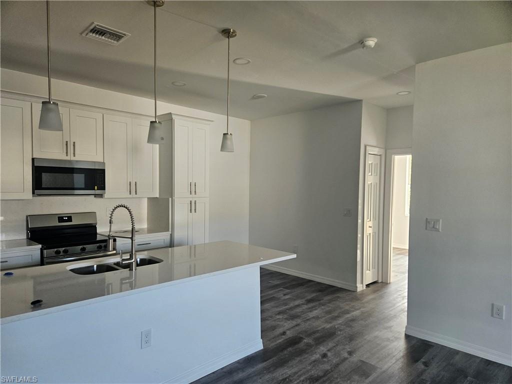 Kitchen featuring appliances with stainless steel finishes, a sink, dark wood-style flooring, white cabinetry, and hanging light fixtures