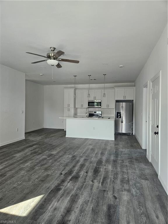 Unfurnished living room featuring dark wood finished floors, ceiling fan, baseboards, and a sink