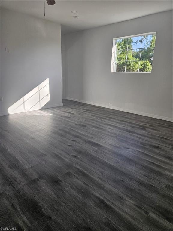 Spare room featuring baseboards, dark wood-style floors, and a ceiling fan