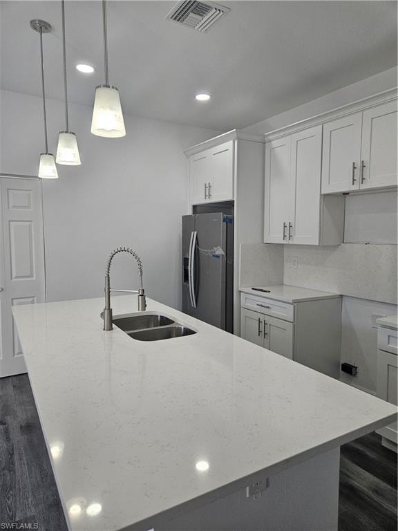 Kitchen featuring an island with sink, a sink, stainless steel fridge with ice dispenser, light stone countertops, and visible vents