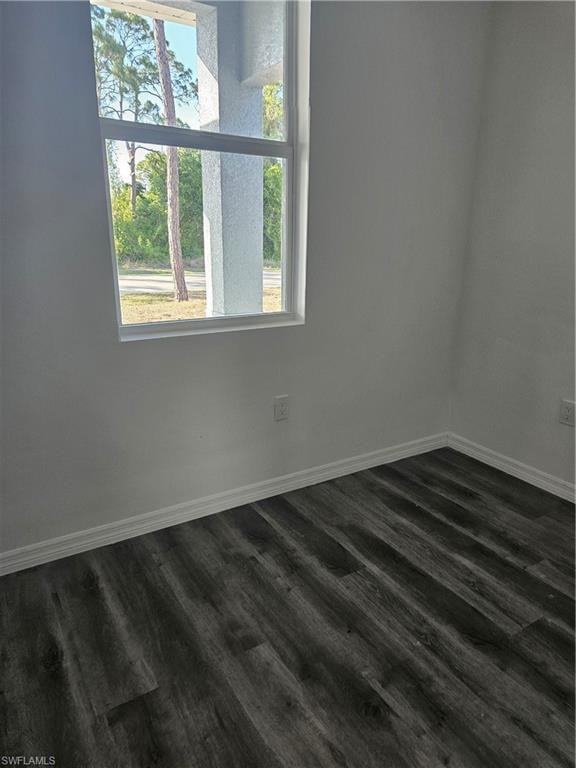 Spare room featuring baseboards and dark wood-style flooring