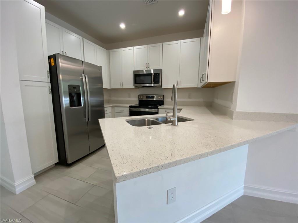 Modern kitchen featuring white shaker cabinetry, stainless steel appliances, speckled quartz countertops, and a double basin sink with a gooseneck faucet