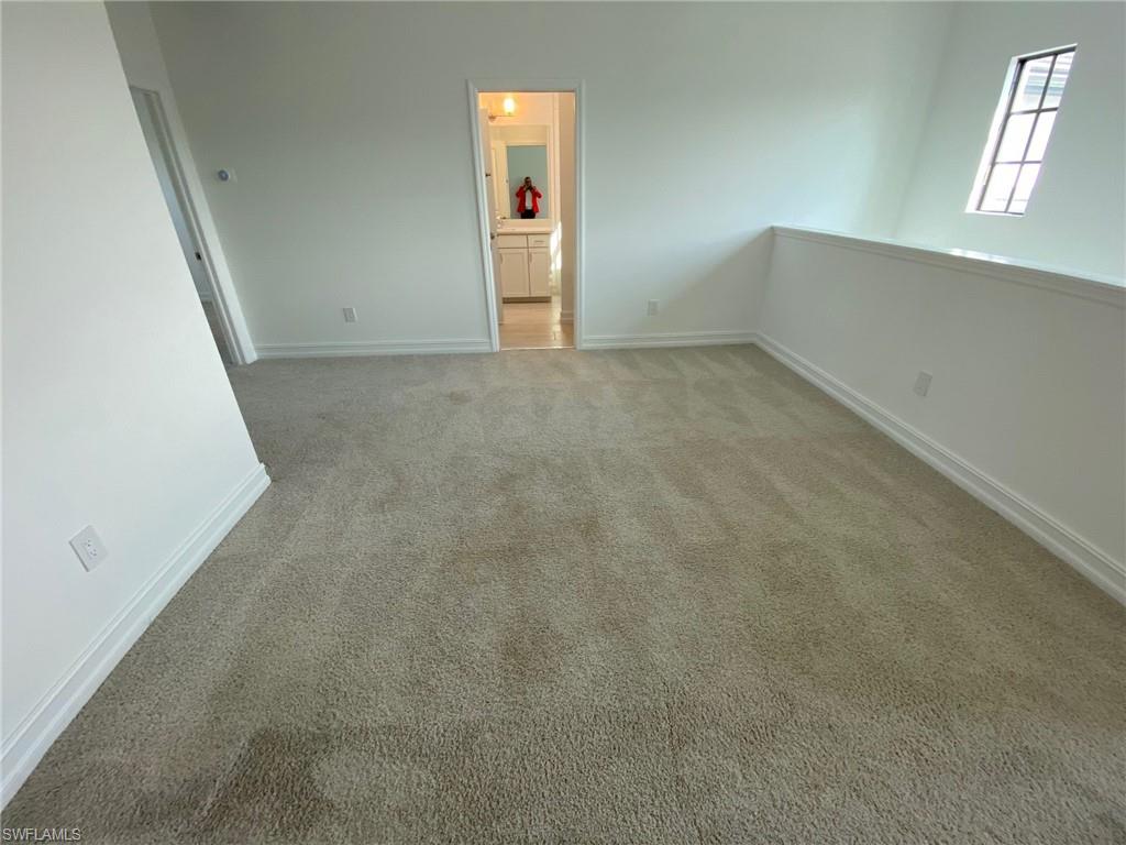 Carpeted open area with white walls and baseboards