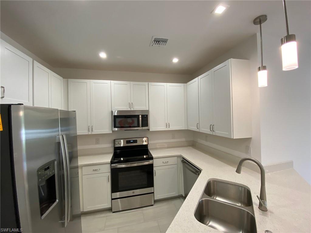 Modern kitchen featuring white shaker cabinetry, stainless steel appliances, light-toned countertops, a double basin sink, and recessed lighting with pendant fixtures