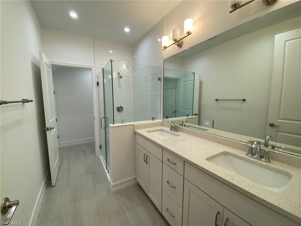 Spacious bathroom featuring a dual vanity with ample countertop space, a large mirrored wall, a glass-enclosed shower with subway tile surround, recessed lighting, and tile flooring
