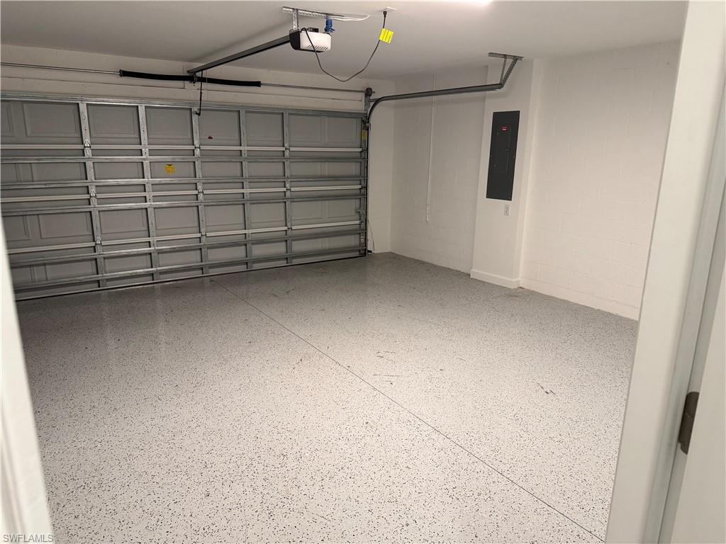 Spacious garage featuring a durable epoxy-coated floor, automatic garage door opener, and a wall-mounted electrical panel