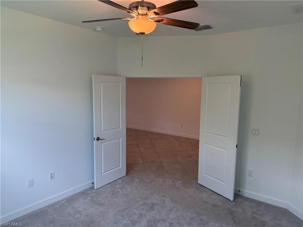 Carpeted room featuring a ceiling fan with light fixture and white shaker-style double doors opening to a tiled interior space