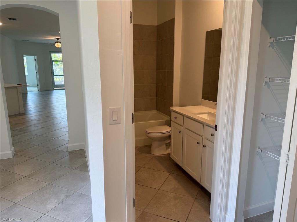 Bathroom featuring a white vanity with integrated sink, a rectangular mirror, a bathtub with tiled surround, and diagonal tile flooring