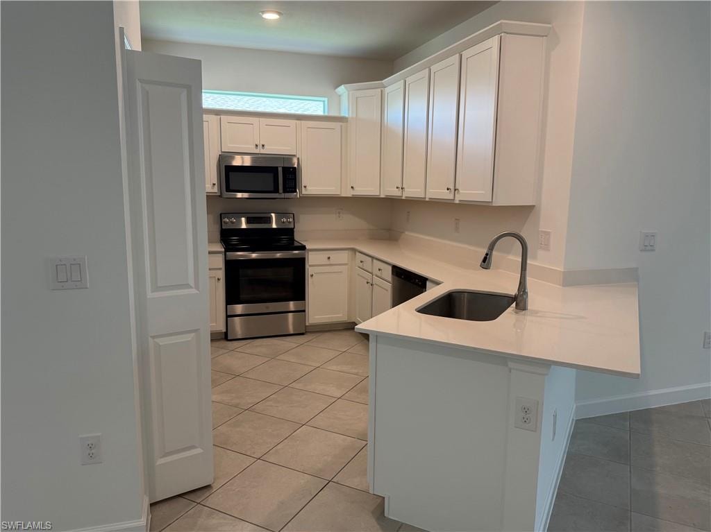 Kitchen featuring white cabinetry, stainless steel appliances, light-toned countertops, a stainless steel sink with a gooseneck faucet, and tile flooring