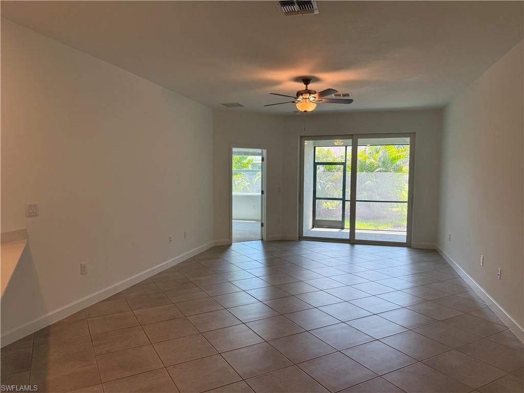 Bright interior space featuring neutral tile flooring, a ceiling fan with integrated lighting, and white baseboards
