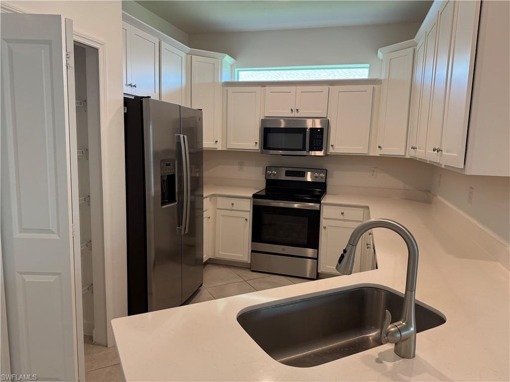 Contemporary kitchen featuring white cabinetry, stainless steel appliances, light-toned countertops, a stainless steel undermount sink, and a pantry with wire shelving
