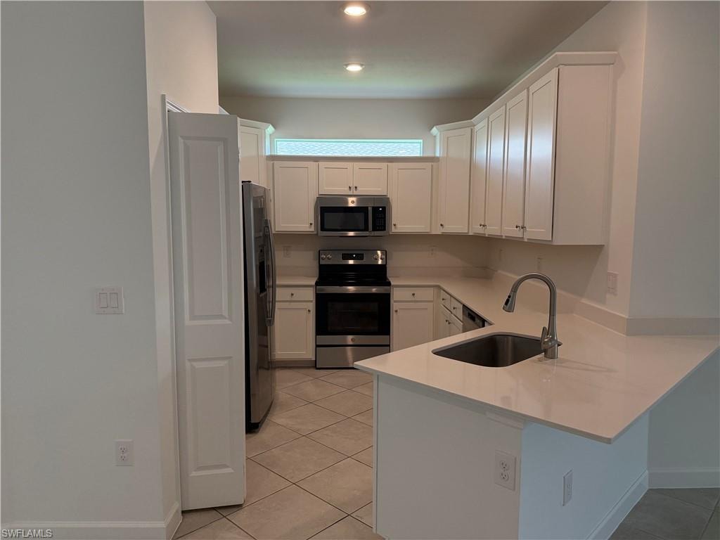 Kitchen featuring white cabinetry, stainless steel appliances, a stainless steel sink with a gooseneck faucet, light countertops, and tile flooring