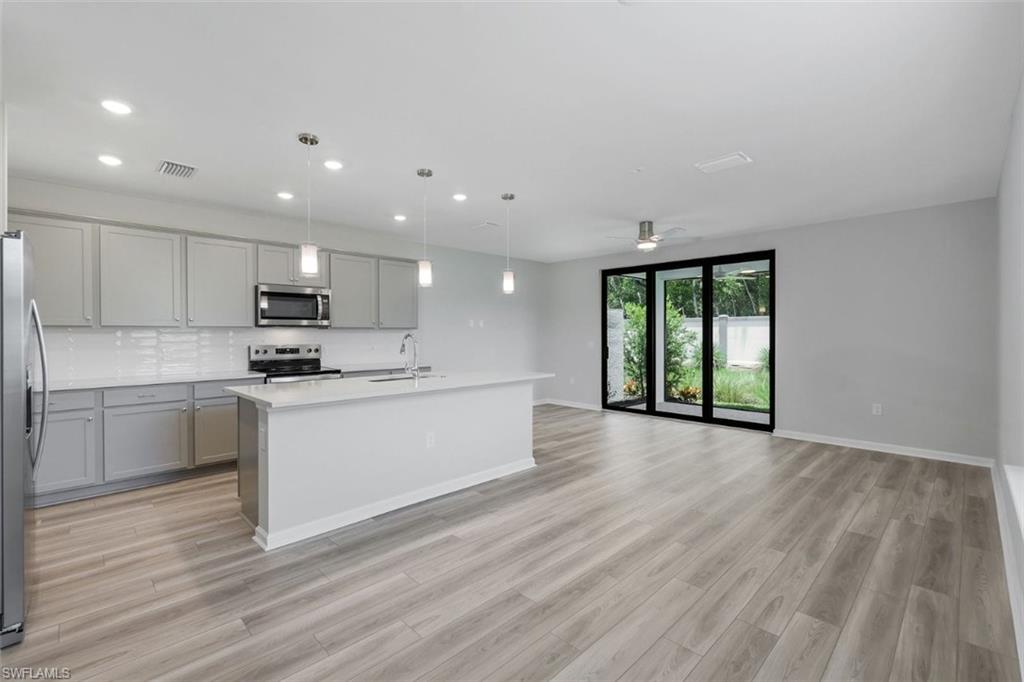 Open-concept kitchen and living area featuring wood-finish flooring, a kitchen island with pendant lighting, stainless steel appliances, and sliding glass patio doors
