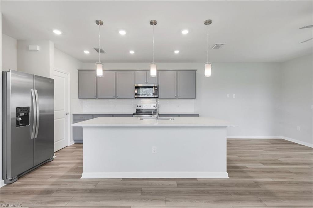 Modern kitchen featuring a central island with a solid surface countertop, stainless steel appliances, gray cabinetry, and wood-finish flooring