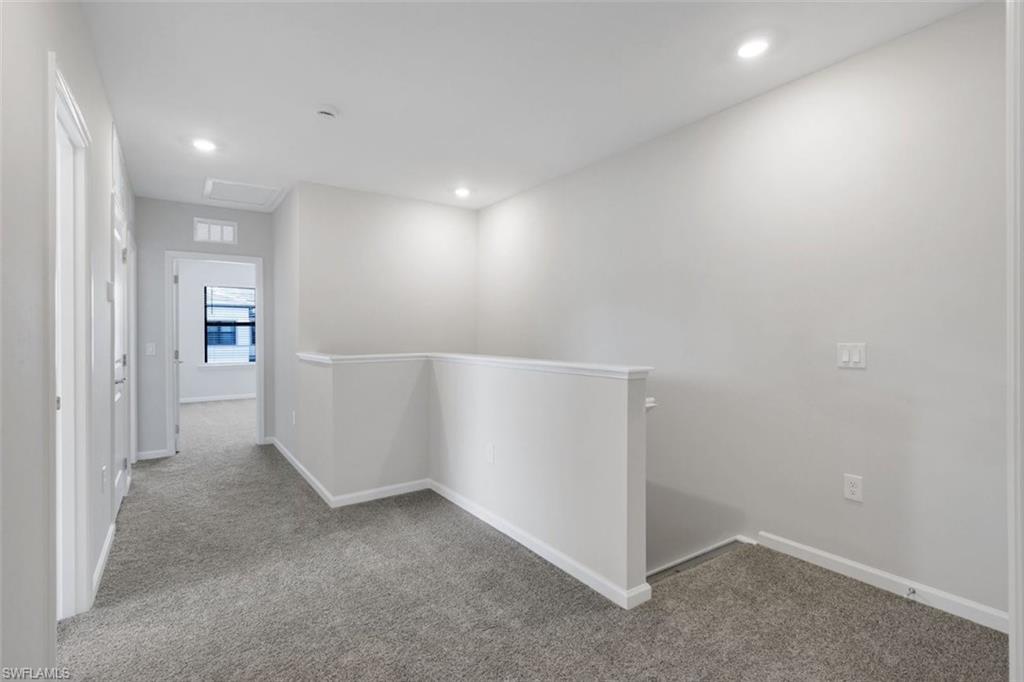 Upper-level hallway featuring plush gray carpeting, recessed ceiling lighting, and crisp white trim