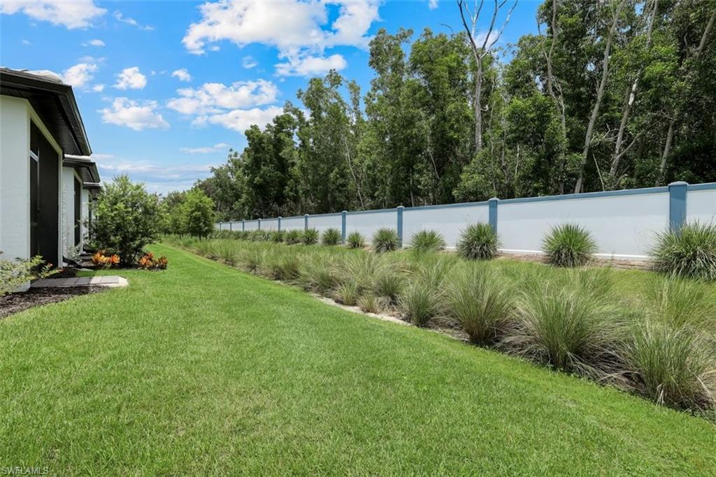 Expansive green lawn bordering a stucco exterior with a dark roofline, featuring a white privacy wall with blue accents, and diverse shrubbery