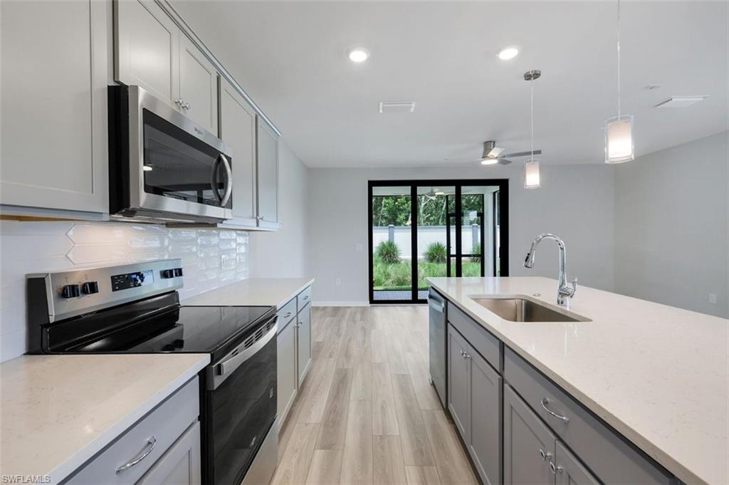 Modern kitchen featuring light gray cabinetry, white countertops, stainless steel appliances, and wood-finish flooring