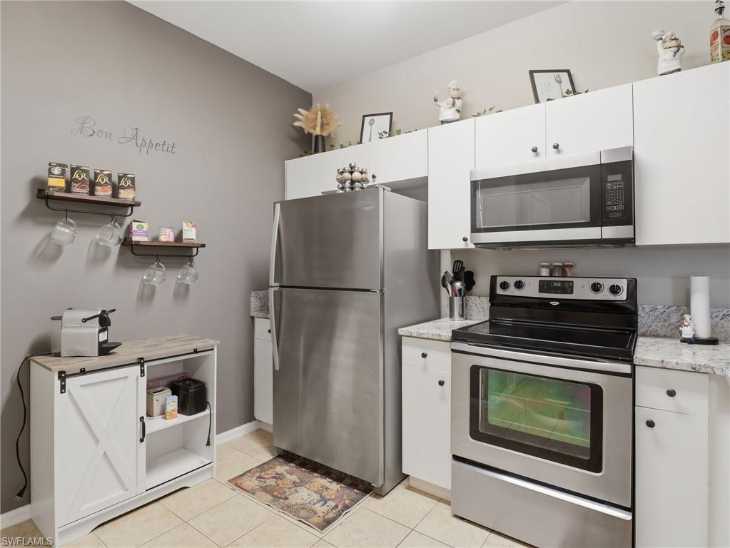 Modern kitchen featuring white cabinetry, stainless steel appliances, granite-style countertops, and tile flooring